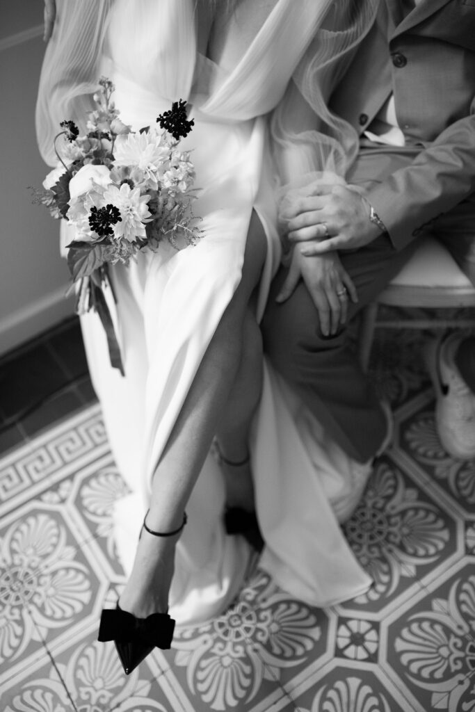 à la villa des Hêtres Pourpres, en alsace, lors de l'immersion mariage, un couple est assis pour la cérémonie laïque. portrait sur le bouquet de la mariée et la fente de sa robe, et les mains du couple. ambiance douce et romantique, photo en noir et blanc