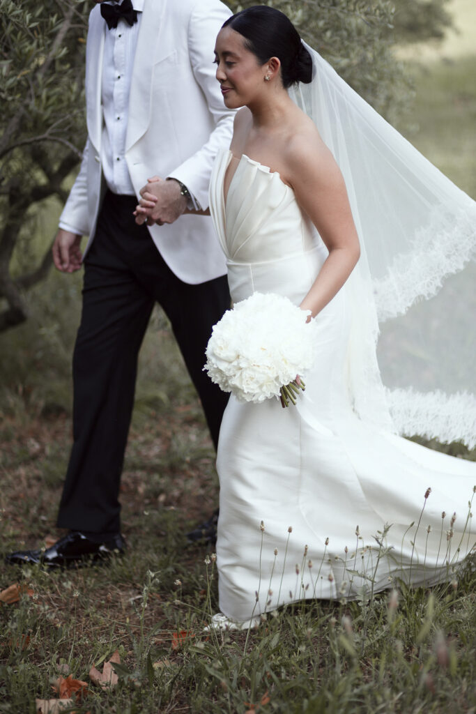 le couple de mariés marche main dans la main, dans les champs d'oliviers dans le sud de la france. le style st naturel et la mise en valeur est sur le bouquet de la mariée