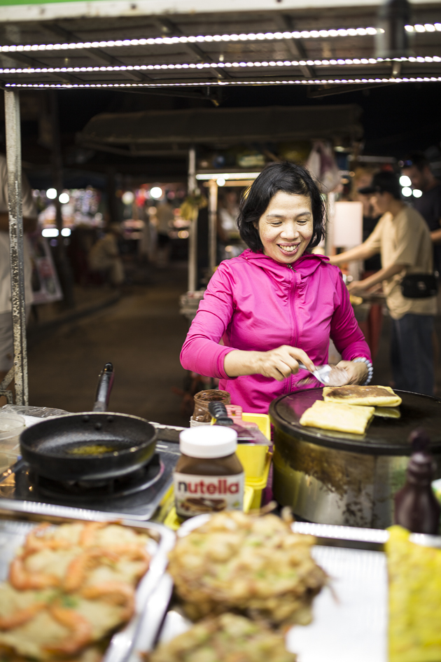 sur un marché vietnamien en soirée, une dame vend des crêpes