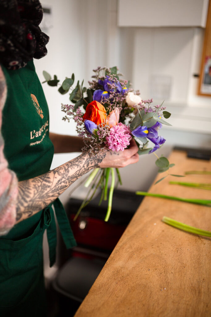 Artisane fleuriste assemblant des fleurs variées pour un bouquet sur mesure.