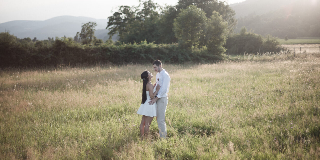 Deux jeunes mariés se tiennent proches dans un champ de hautes herbes au coucher du soleil, partageant un moment intime et paisible